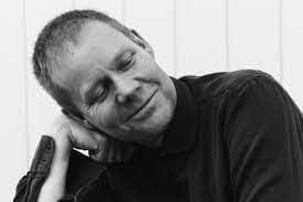 max richter - the departure - piped through the streets in Hobart 2023. A black and white photo of Max Richter leaning on his hand with a gentle, friendly smile on his face