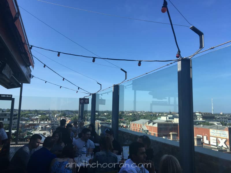 Naked for Satan, views of buildings with sun and people bubbly drinking