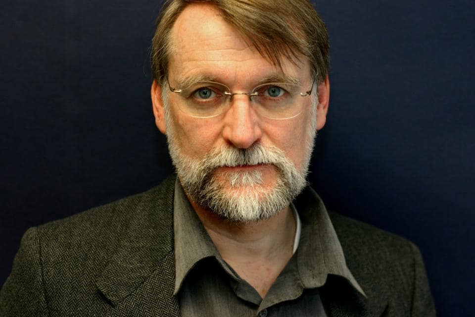 picture of man in brown suit with glasses looking at the camera